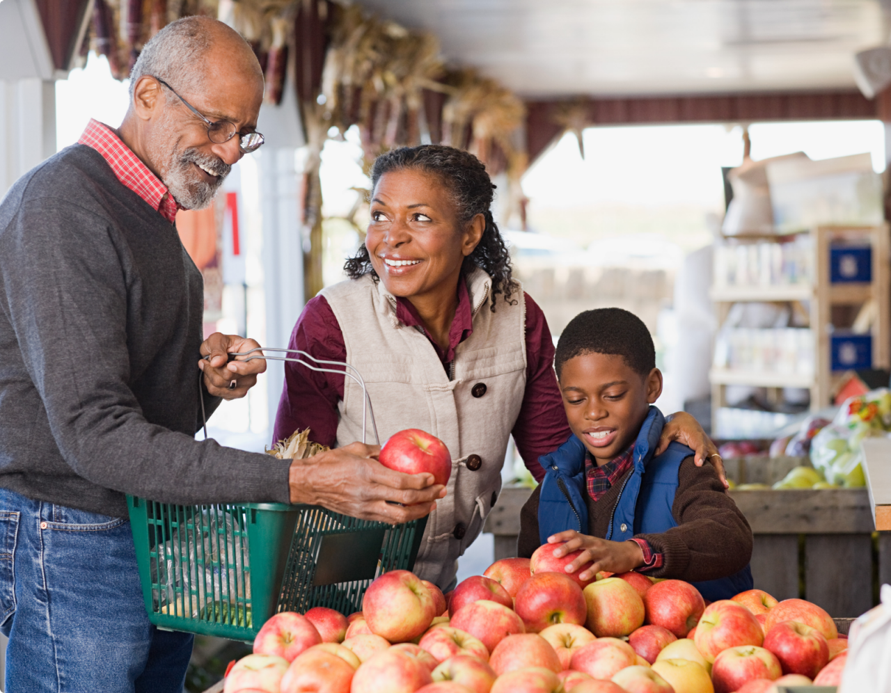 Young boy sitting in his pregnant mother's lap looking at fresh vegetables in the kitchen.