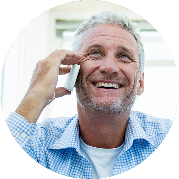 Mature man smiles while talking on mobile phone indoors.