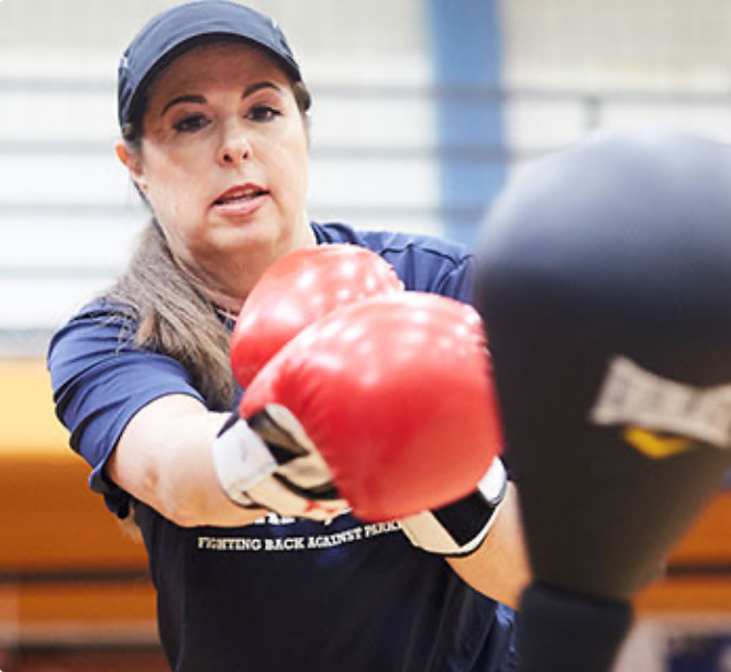 A woman in boxing gloves punching a punching bag.