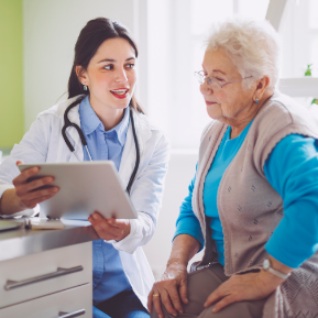 Female doctor holds tablet while talking to senior female patient.