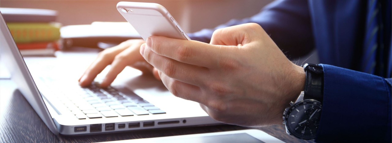 Hands typing on computer and holding cell phone