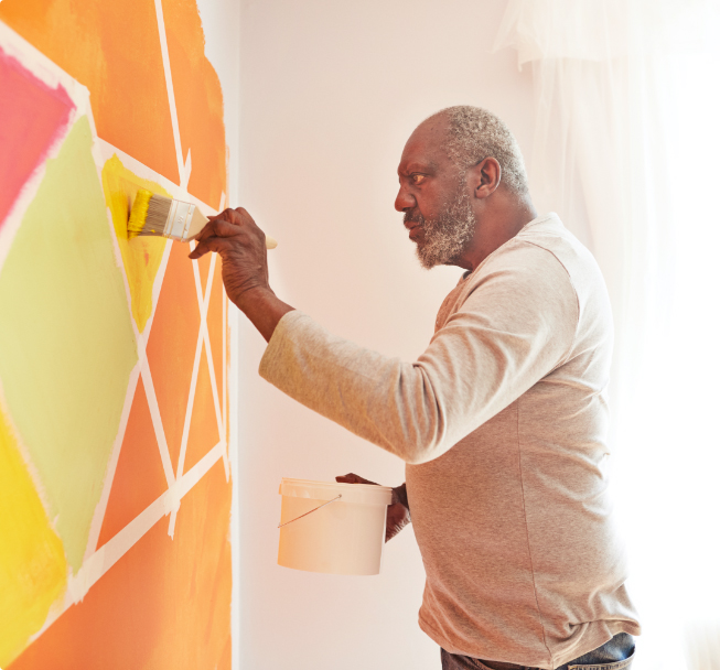 Elderly man painting design on a wall.