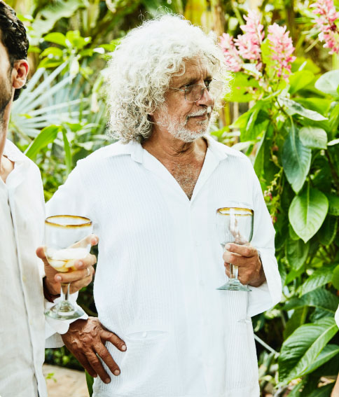 Older man in a garden holding a drink.