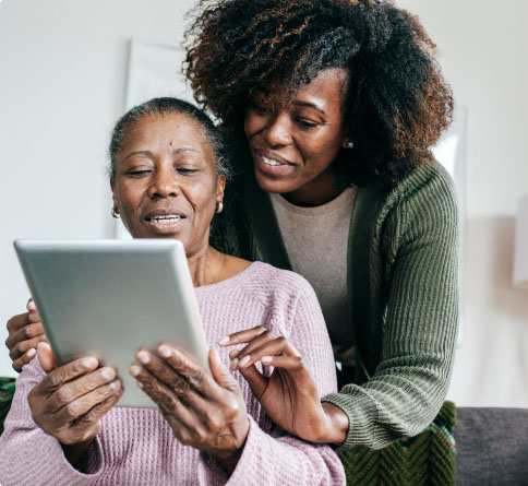 A younger woman helping an older woman on a tablet.