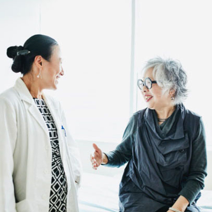 Smiling senior female patient in discussion with doctor during consultation in exam room.